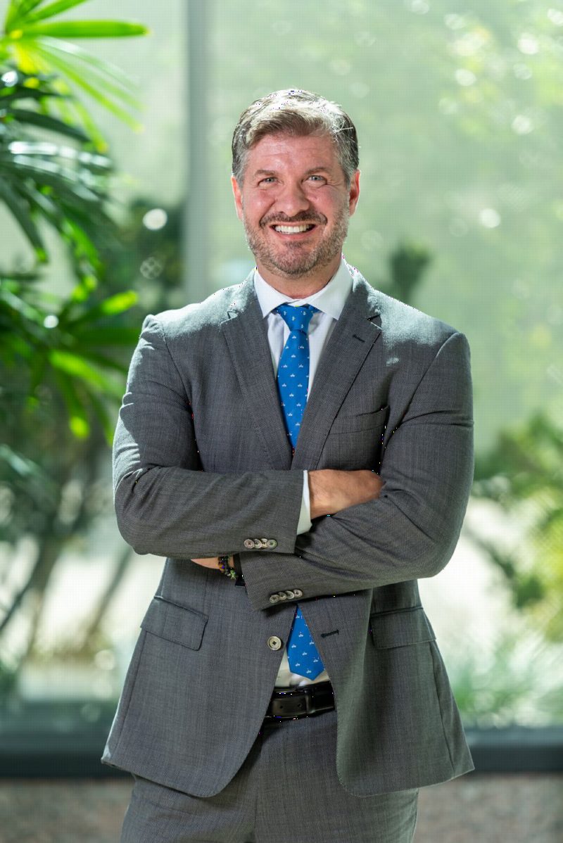 Gui Gatti, con traje gris y corbata azul, sonriendo con los brazos cruzados